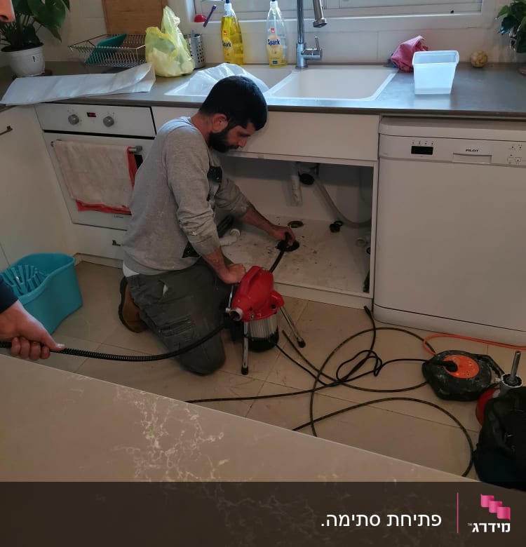 אדם מתקן צנרת מתחת לכיור במטבח